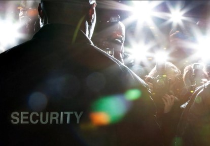 Security guard facing a crowd with intense camera flashes.