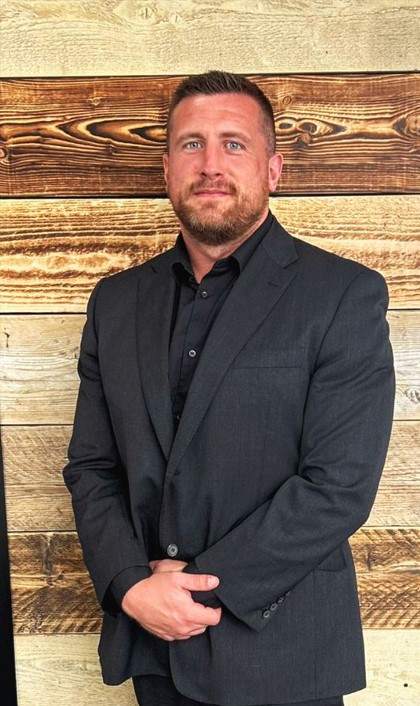 Professional portrait of a man in a dark suit against a wooden background.