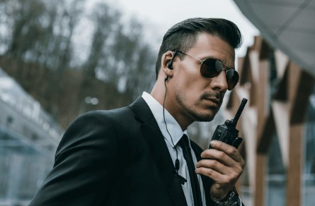Close protection officer in sunglasses and suit holding a radio.